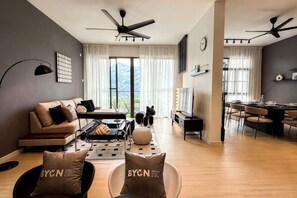 Uma sala de estar moderna com sofá, mesa de centro e cadeiras, uma área de jantar com mesa e cadeiras, e uma janela grande com cortinas.