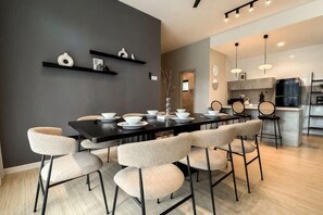 A modern dining area with a black table, beige chairs, and a grey accent wall. - Enclave Nature Suites Bukit Tinggi by BYON (Bentong)