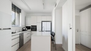 A modern kitchen with white cabinetry, a central island, and a dining area with a chair. - Penthouse - Four Bedroom Apartment, Sleeps 19 (Jerusalem)