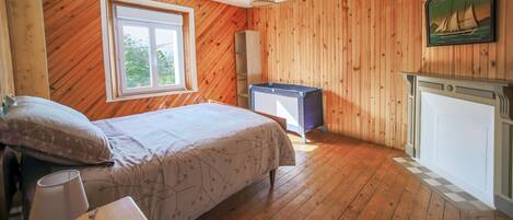 Een slaapkamer met houten wanden, een bed, een nachtkastje, een lamp, een dressoir, een raam en een schilderij van een zeilboot.