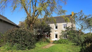 A two-story house with a visible front door, a small garden with a pathway leading to the door, and a tree in the foreground. - 3 bedroom stunning home in Plougasnou (Plougasnou)