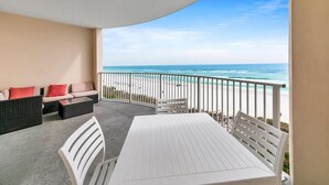 A balcony with a white table and chairs, a sofa with red cushions, and a view of the beach and ocean. - Twin Palms 603 (Panama City Beach)