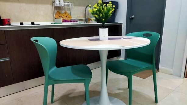 A small round table with two chairs, a white vase with yellow flowers, and a kitchen counter with various items. - Sliverscape Premier Suite @ Melaka Raya [Bathtub Sleep 2-4] (Melaka)