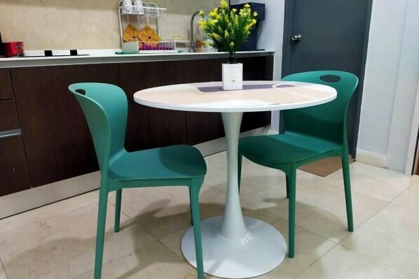 Une petite table ronde avec deux chaises, un vase blanc contenant des fleurs jaunes et un comptoir de cuisine avec divers objets.