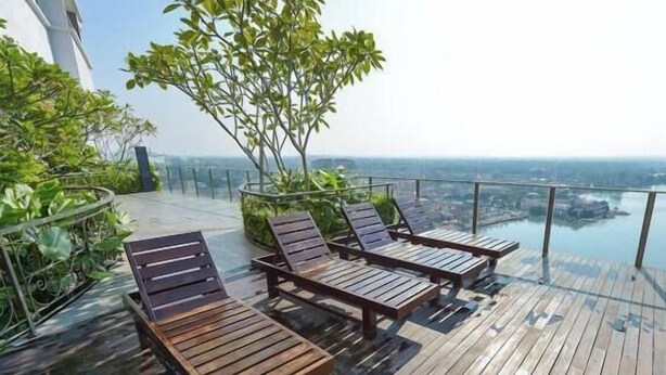 Een dak terras met houten lounge fauteuils en een glazen balustrade met uitzicht op een stadsbeeld.