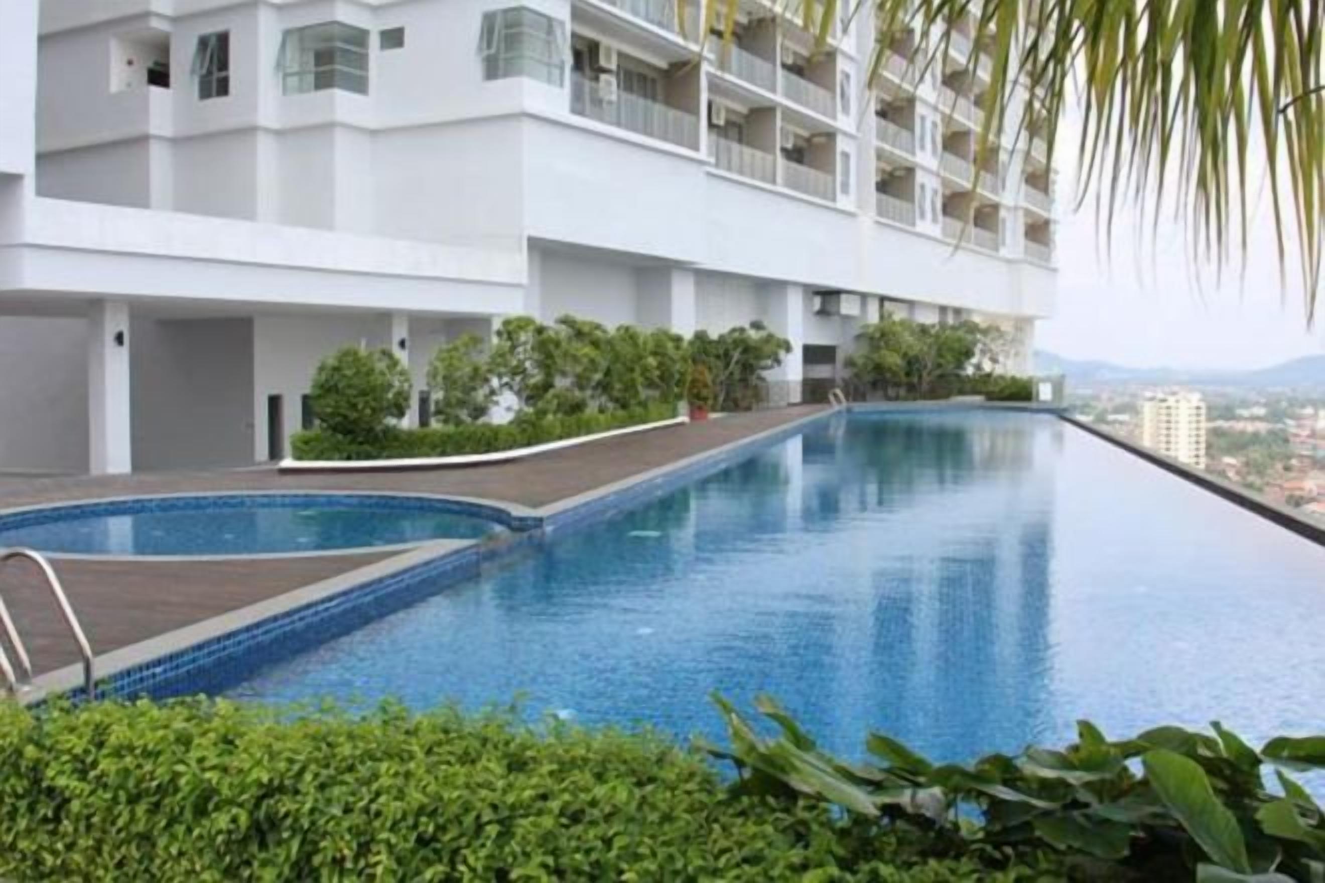 A swimming pool adjacent to a white building with balconies, surrounded by greenery.