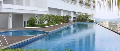 Una piscina junto a un edificio blanco con balcones, rodeada de vegetación.