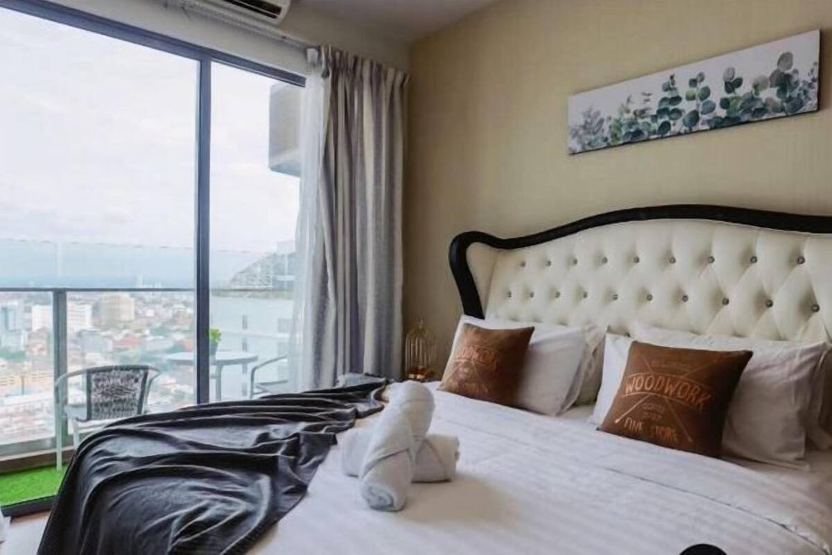 Une chambre d’hôtel dotée d’une grande fenêtre donnant sur la ville, d’une tête de lit capitonnée et d’un lit agrémenté d’oreillers soigneusement disposés.