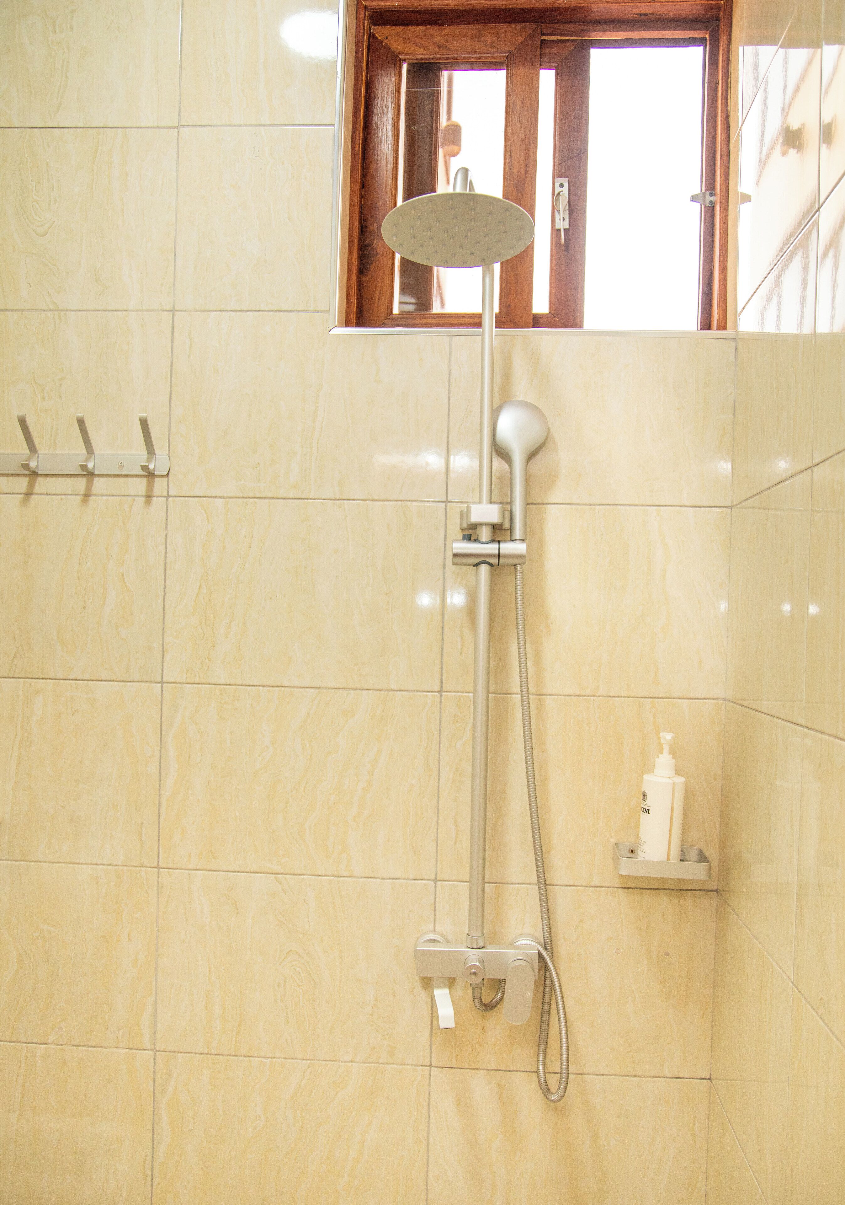 Een badkamer met een douche, een raam en een zeepdispenser op een plank.