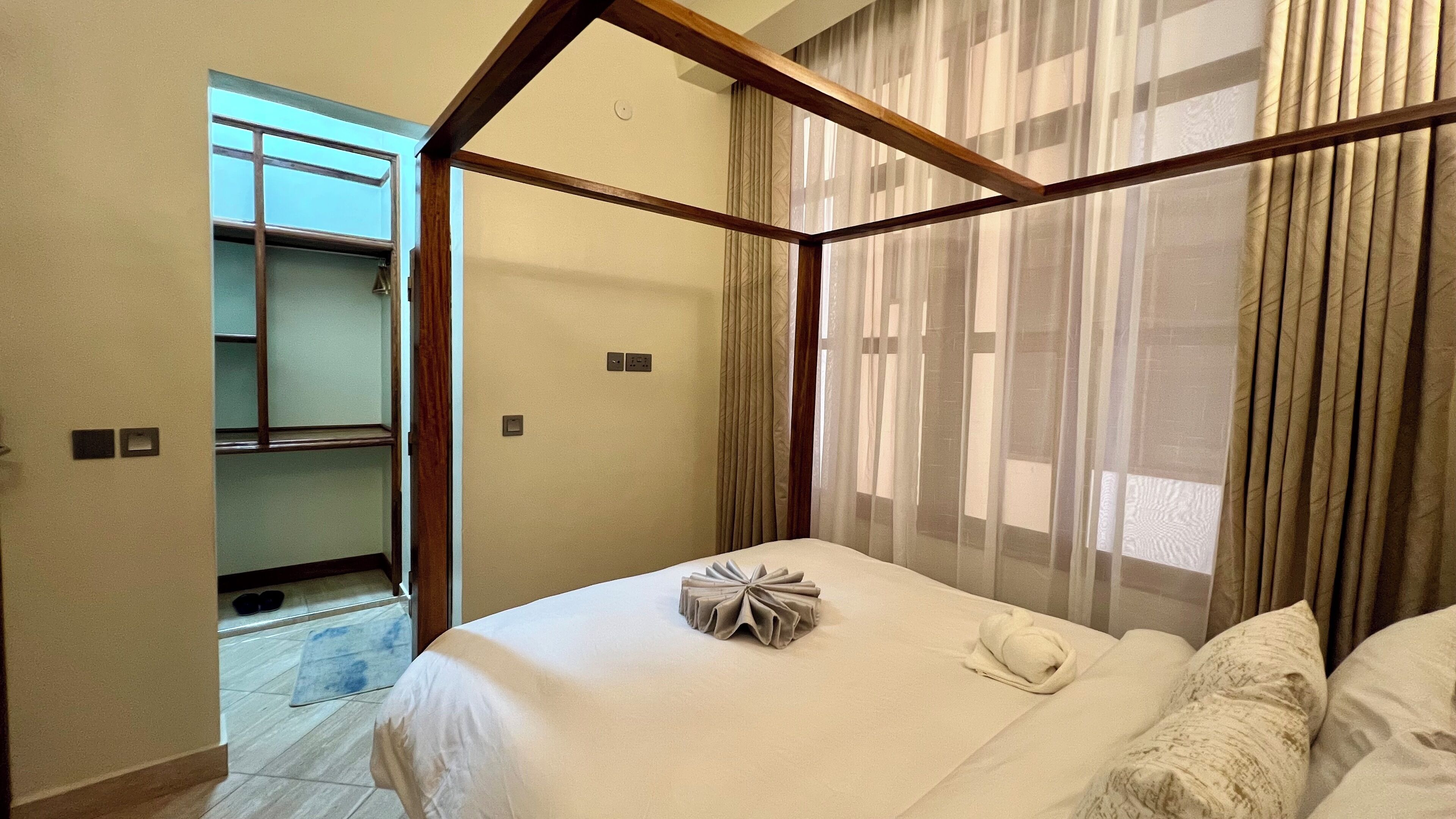 Une chambre à coucher avec un lit à baldaquin, une petite salle de bain et une vue sur l’extérieur à travers des rideaux transparents.