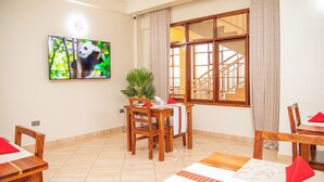 Comedor con muebles de madera, un televisor mostrando un panda y vista a una escalera.