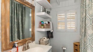 A bathroom with a wooden vanity, a large mirror, a white sink, and a toilet. There are shelves above the sink with toiletries and a window with shutters. - 3-bedroom Lake Martin, AL cabin in cool Equality with WiFi, AC (Equality)