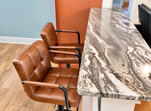 Una silla de cuero marrón con reposabrazos y estructura metálica negra, ubicada al lado de una mesa de mármol con diseño blanco y gris.