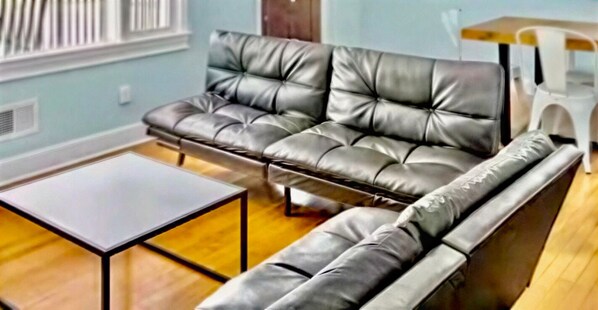 Una habitación con sofá de cuero, una mesita y suelo de madera.