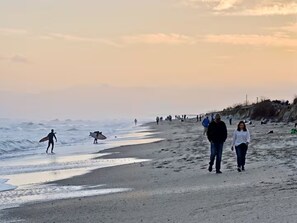 Una playa con gente caminando y practicando surf, y un muelle al fondo.