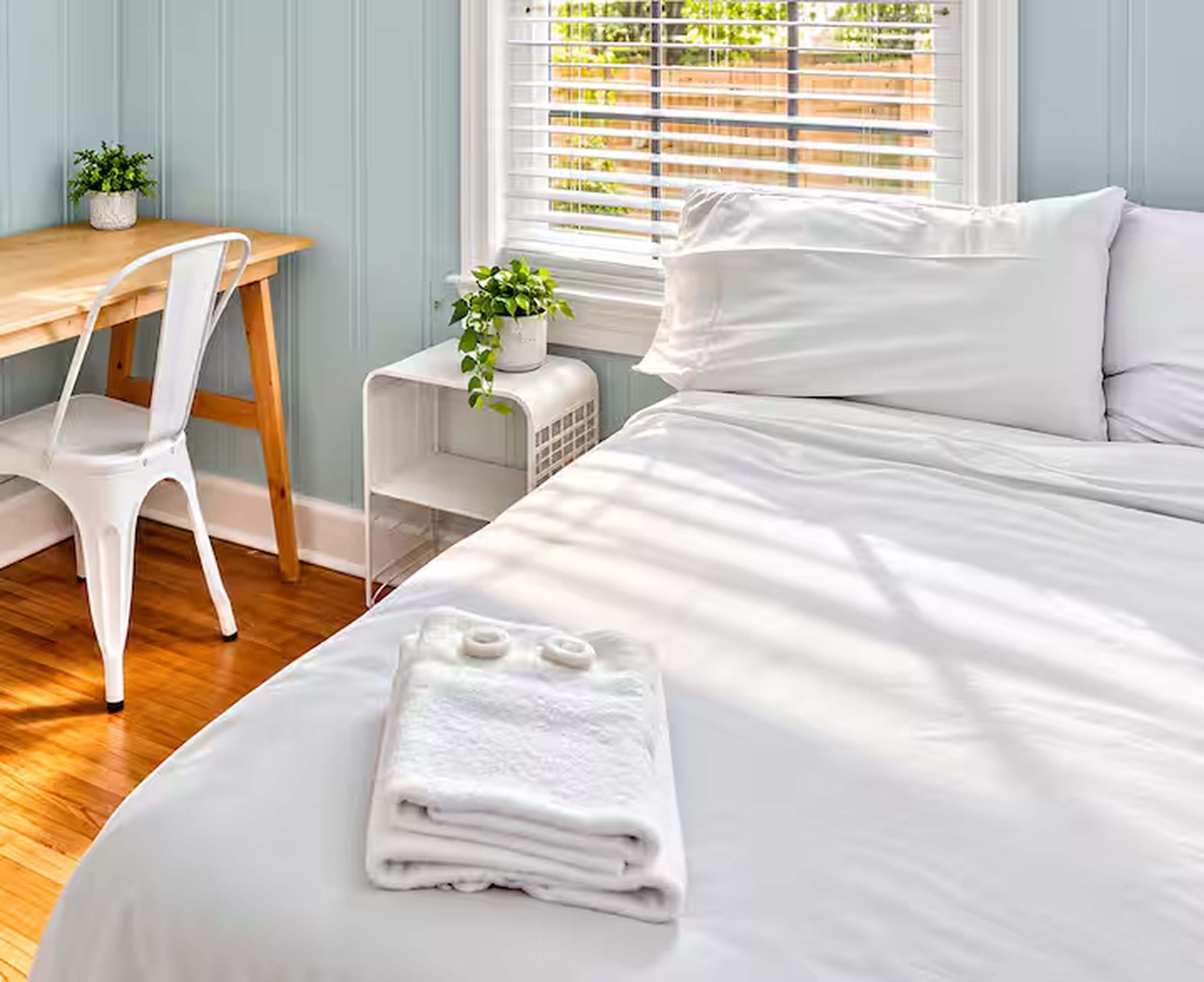 Een hotelkamer met een bed, een bureau, een stoel, een radiator en een raam met zonwering.