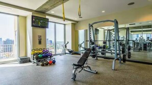 A gym with exercise equipment, a bench, kettlebells, and a large window with a city view. - 19th Floor Midtown Sky Suite | Free Parking | Gym (Atlanta)