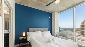A modern hotel room with a large bed, a nightstand, a chair, and a city view through large windows. - 19th Floor Midtown Sky Suite | Free Parking | Gym (Atlanta)
