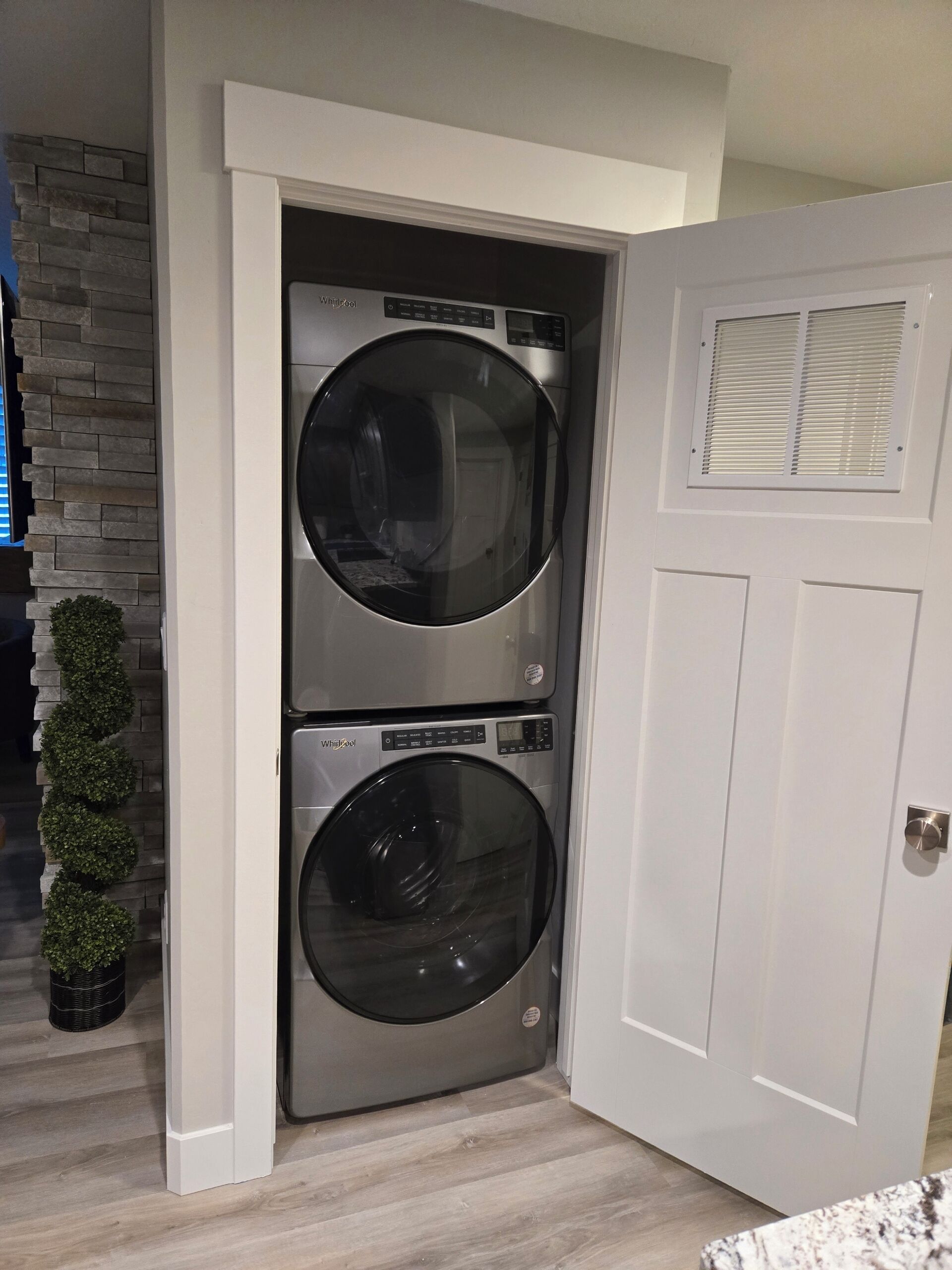 A compact laundry room with two stacked front-loading washers and dryers, a white door, and a stone accent wall.