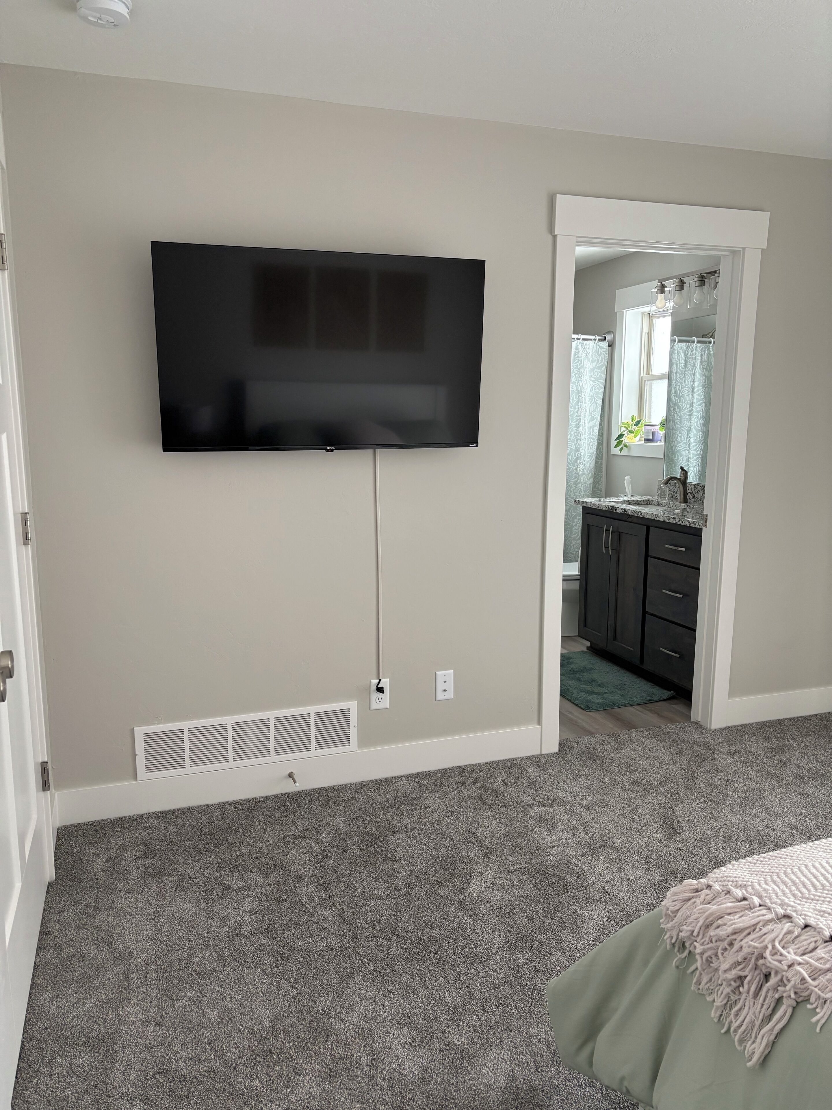 Une chambre dotée d’un téléviseur à écran plat fixé au mur, d’un sol recouvert de moquette et d’une couvre-lit verte.