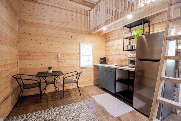 A compact kitchen with wooden walls, a dining table with chairs, a refrigerator, and a window.