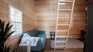 A cozy cabin interior with a wooden interior, a blue sofa, a ladder, a radiator, and a window with a view. - Columba - New Lofted Kabin (Kawartha Lakes)