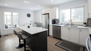 A modern kitchen with a central island, stainless steel appliances, and a large window providing natural light. - Dorado House-Cottage (Kawartha Lakes)