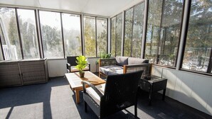 A sunroom with large windows, wicker furniture, and a view of trees. - Dorado House-Cottage (Kawartha Lakes)
