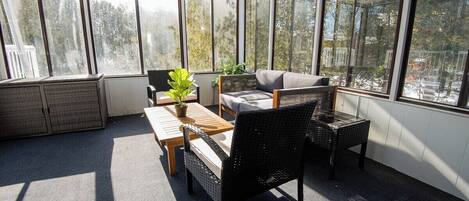 A sunroom with large windows, wicker furniture, and a view of trees.