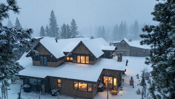 Una cabaña nevada con varias habitaciones, un espacio central abierto y vistas a los árboles circundantes.