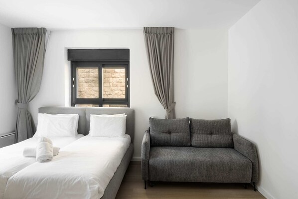 A bedroom with a bed, a grey sofa, and a window with curtains.