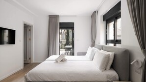 A modern hotel room with a large bed, a TV mounted on the wall, and a balcony with a view of the city.