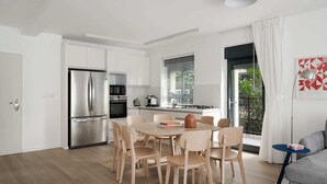 A modern kitchen with stainless steel appliances, a dining area with wooden chairs, and a balcony with a view.