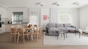 A modern living room with a grey sofa, wooden chairs, a coffee table, and a dining area with a round table and chairs.