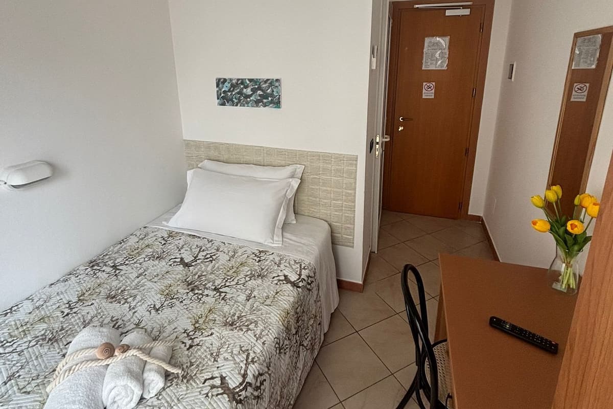 A hotel room with a bed, a desk, a chair, a wall-mounted air conditioner, and a door with a sign.
