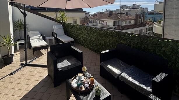 A rooftop terrace with outdoor furniture, a large umbrella, and a view of the cityscape. - Hotel Dream (Rimini)