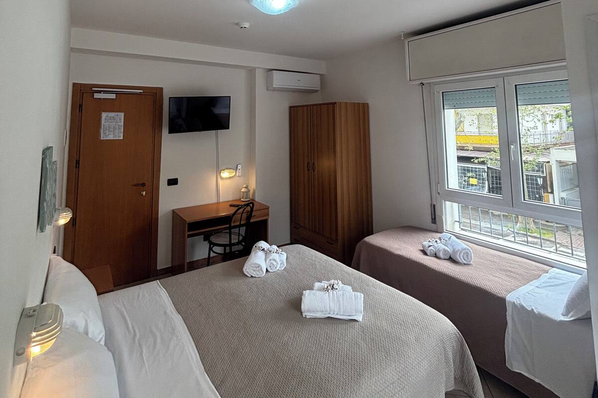 A hotel room with two beds, a desk, a TV, and a window with a view.