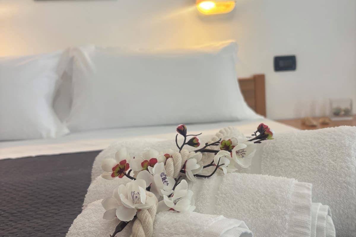 A neatly made bed with white linens, a decorative branch with flowers, and a painting on the wall.