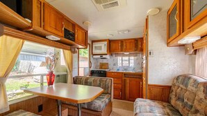 Une cuisine compacte pour camping-car, dotée de meubles en bois, d’un four à micro-ondes et d’un coin repas avec une table et deux sièges rembourrés.