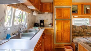 Une cuisine compacte pour camping-car, avec des placards en bois, un évier, une machine à café et un réfrigérateur.
