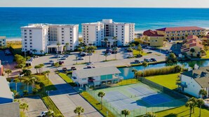 A beachfront hotel with multiple white buildings, a parking lot, and a tennis court. - GULF FRONT relaxing condo on GORGEOUS Pensacola Beach. Private pool,low density! (Gulf Breeze)