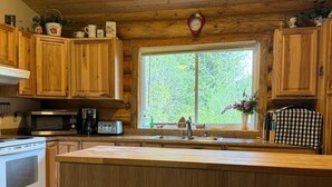 Une cuisine avec des meubles de rangement en bois, une grande fenêtre, un évier et une cuisinière.