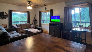Un salon chaleureux avec un plafond en bois, un ventilateur de plafond, un téléviseur et un coin repas comprenant une table et des chaises.