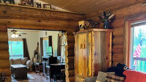 L’intérieur d’un chalet accueillant, avec un plancher en bois, un canapé, une table basse, un coin repas et une grande armoire en bois.