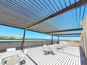 An outdoor terrace with a view of the ocean, featuring a covered seating area with tables and chairs.