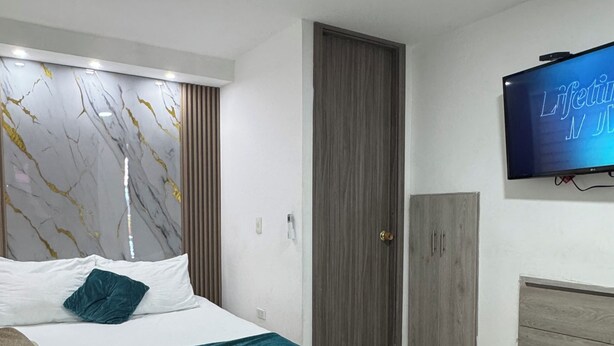 A modern bedroom with a bed, a TV, a wardrobe, and a door.