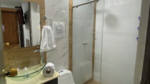 A modern bathroom with a glass shower enclosure, a white toilet, a glass sink with a marble backsplash, and a wooden vanity.