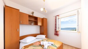 Ein Schlafzimmer mit Bett, Holzschrank, Fenster mit Aussicht und Deckenleuchte.