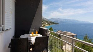 Ein Balkon mit Tisch für zwei Personen, mit Blick auf die Küste und Berge in der Ferne.