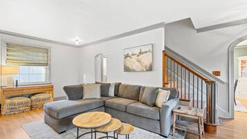 A modern living room with a sectional sofa, a wooden coffee table, and a staircase.